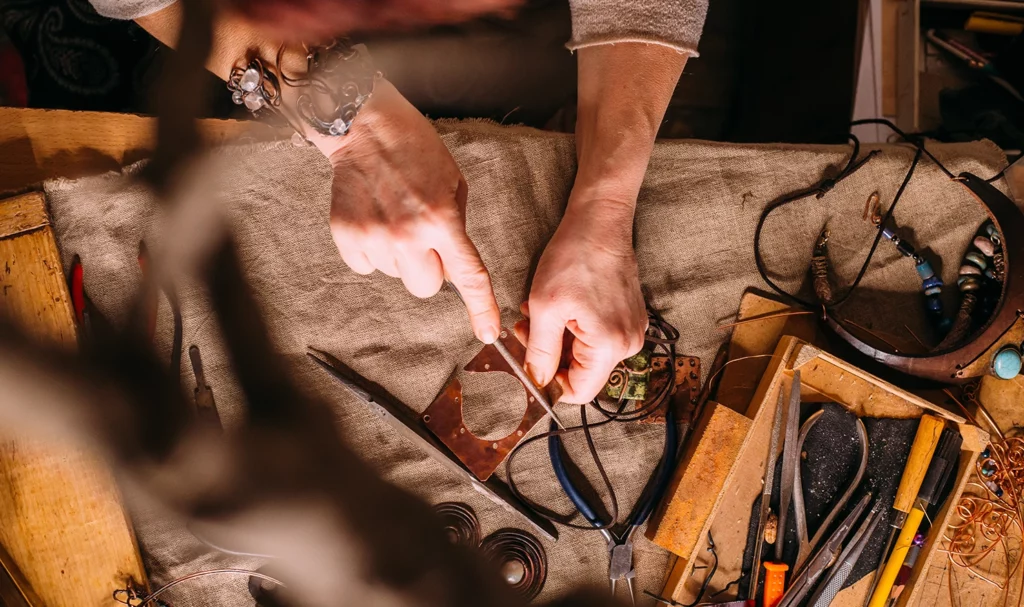Overhead view of a leather worker using tools and copper wire on a workbench in a studio.