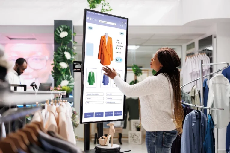 a woman browsing a clothing catalog on a large touchscreen kiosk inside a clothing boutique