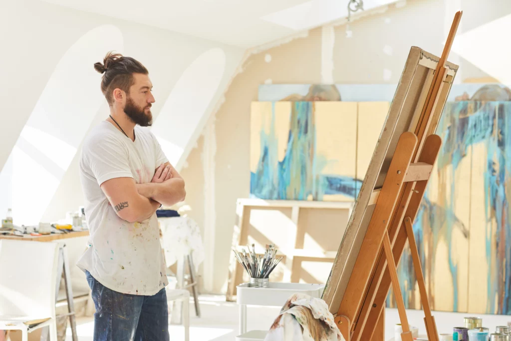 a male artist reflects on his work inside a painting studio