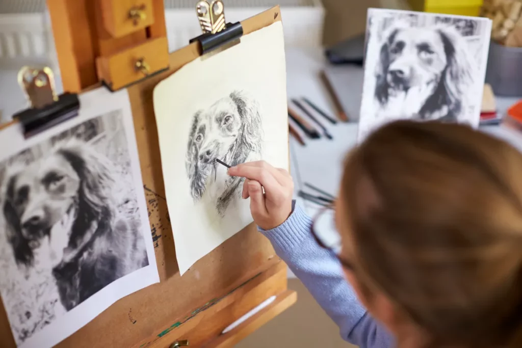 An artist sketches a black-and-white portrait of a dog on a wooden easel.