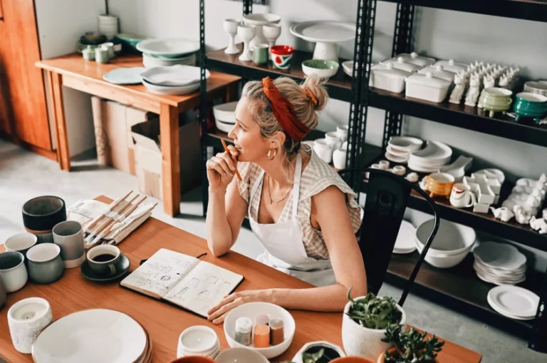 a female pottery artist sitting in her workshop, thinking over an open journal